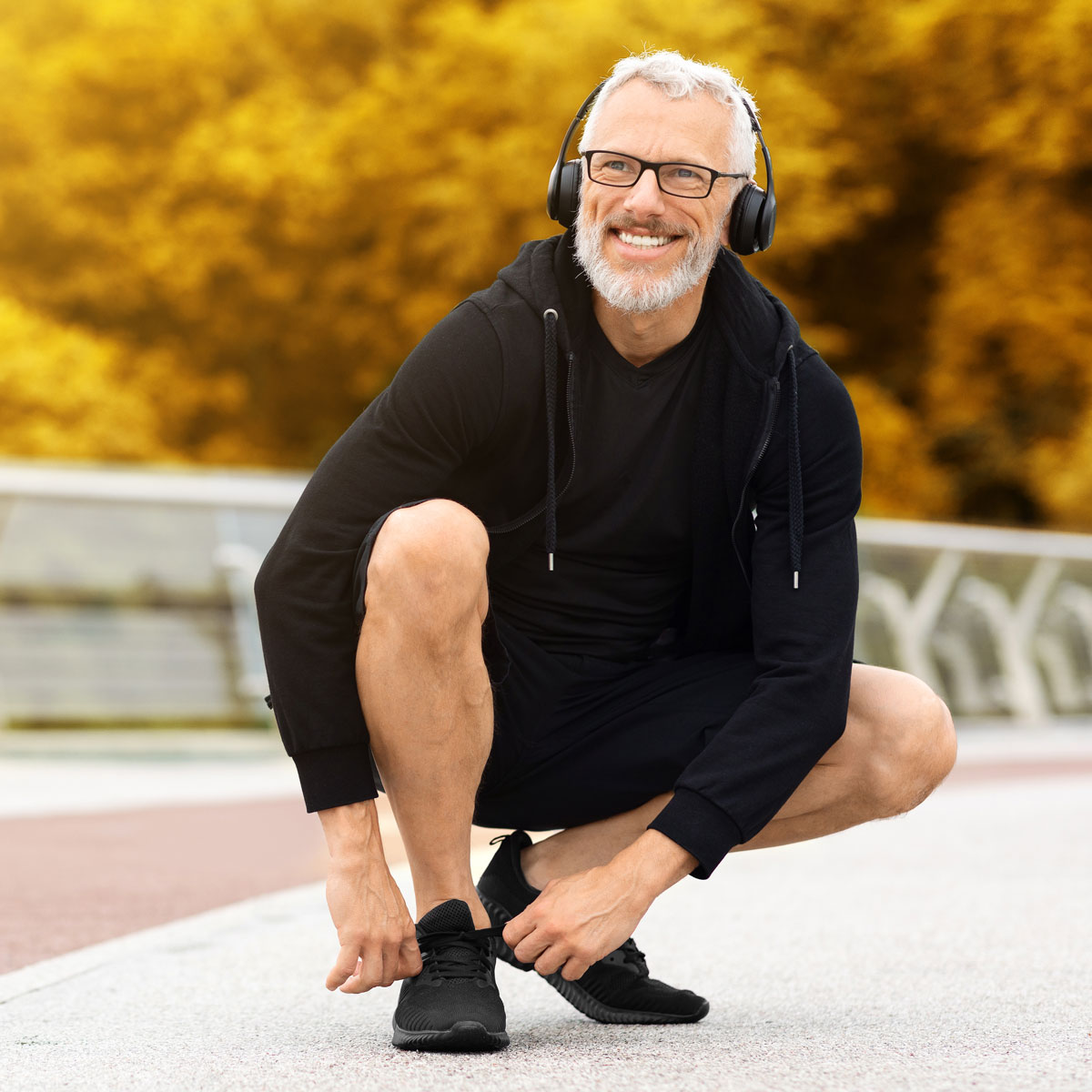 Man in running clothers kneeling to tie shoe laces on a running path surrounded by trees.