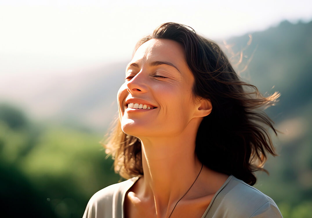 Photo of middle age woman smiling with eyes closed facing the sun.