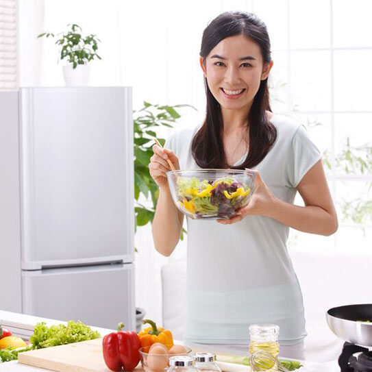 Photo of a woman standing behind kitchen counter holding a glass bowl of salad