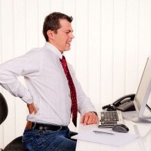 Photo of a man at a desk with his hand reaching behind to support his back