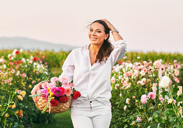 Photo of smiling woman in field holding basket of flowers.